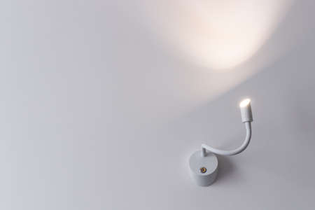 White lamp on a white color painted wall. WAll lamp is on.