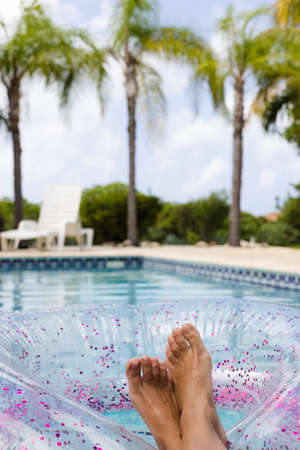 Female feet on a rubber ring with glitter in it in swimming pool with view to the palm trees. Woman...