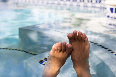 Female feet in water in swimming pool, closeup. Woman relaxing near swimming pool. Holidays, beauty, foot care concept.の写真素材