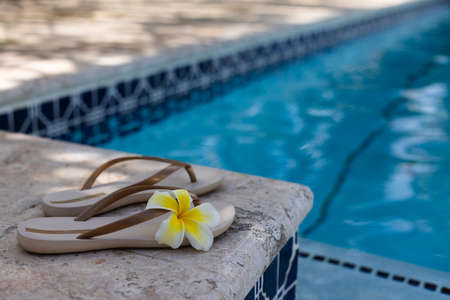 Slippers with frangipani flowers near swimming pool. Closeup, selective focus.の写真素材