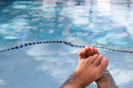 Female feet in water in swimming pool, closeup. Woman relaxing near swimming pool. Holidays, beauty,...