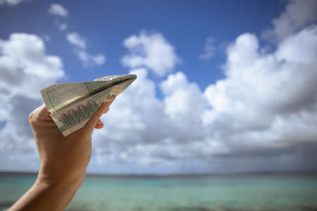 Hand holding the plane made of 1000 Armenian bills on a background of the seascape.