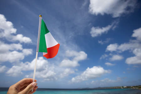 Female hand holding Italian flag on the background of the seascape.
