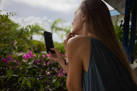 Dreaming girl with telephone on a balcony with a view to the tropical garden.