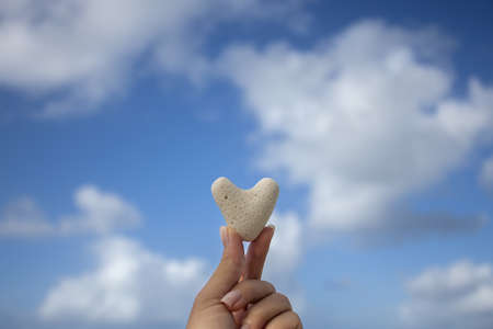 Female hand holding small heart from coral on the background of the seascape.の写真素材