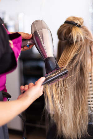 Drying blond hair with hair dryer and round brush at hairdresser.の写真素材