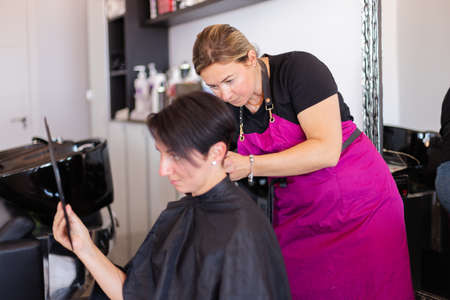 The woman examines her haircut in the mirror at the hairdresser.の写真素材