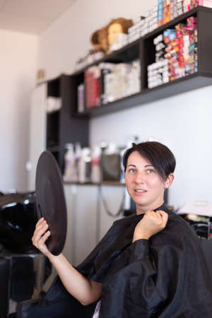 The woman examines her haircut in the mirror at the hairdresser.の写真素材