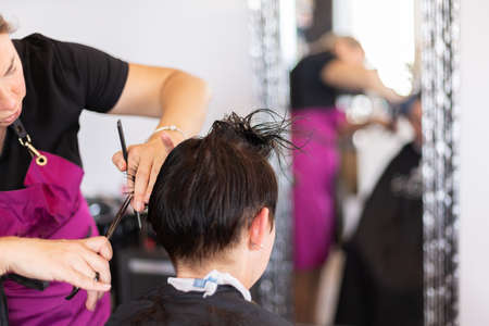 Hairdresser cutting and modelling brown hair by scissors and combの写真素材
