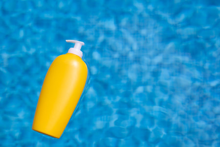 Sunscreen bottle floating in blue water of swimming pool.の写真素材