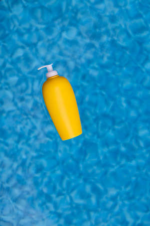 Sunscreen bottle floating in blue water of swimming pool.