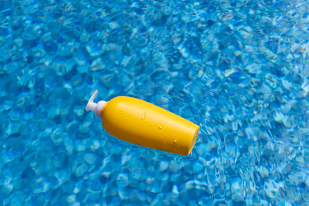 Sunscreen bottle floating in blue water of swimming pool.の写真素材