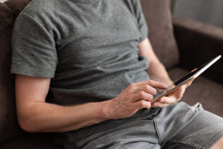 Man sitting on a couch with a tablet in his hands. Using technology.の写真素材