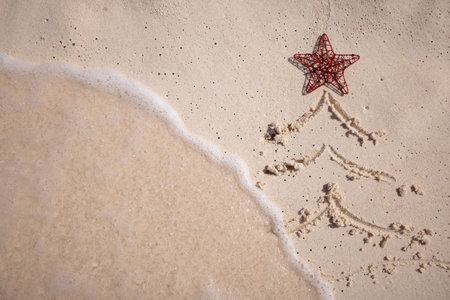 Christmas tree drawn on the sandy beach with red star and the wave is coming close.の写真素材