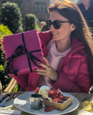 Happy young woman sitting in a cafe outside with Belgian waffles and holding gift box.の写真素材