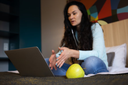 Healthy fruit. Snack during work time. Woman on a bed having videoconference. Selective focus.の写真素材