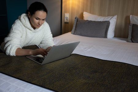 Woman on a bed busy behind laptop. Serious woman working or studying at home behind laptop till late evening.の写真素材