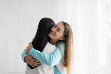 Two best girlfriends hugging embracing near window at home. Girls happy to see each other.の写真素材