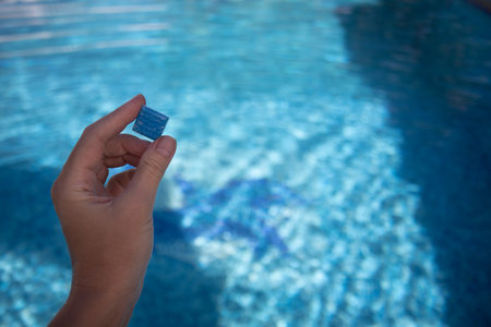 Hand holding small tile from floor of swimming pool. Tile from pool bottom cover.