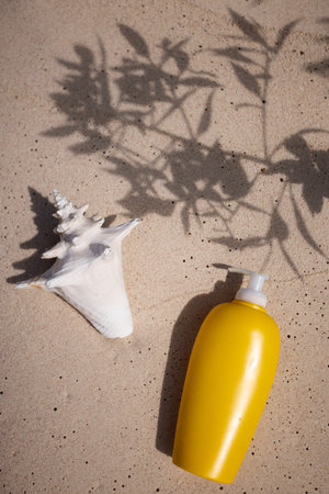 Mockup. Yellow suncream bottle and seashell on the sand in the shadow from leaves. UV and sunburn...