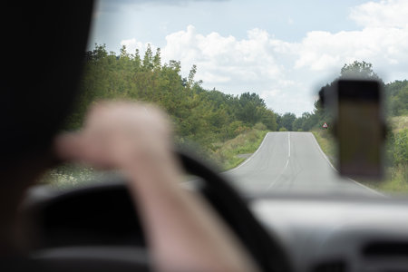 View through the windscreen of the car to the road with road sign and green bushes on both sides of...