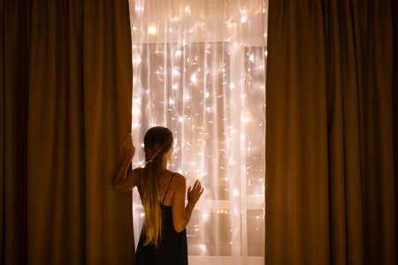 Woman standing near window with Christmas illumination. Christmas holidays concept.の写真素材