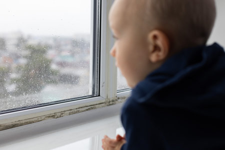 Closeup shoot of little child looking through the window with black spots on it. Selective focus.の写真素材