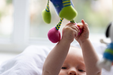Newborn baby playing with hanging toys. Closeup, selective focus.