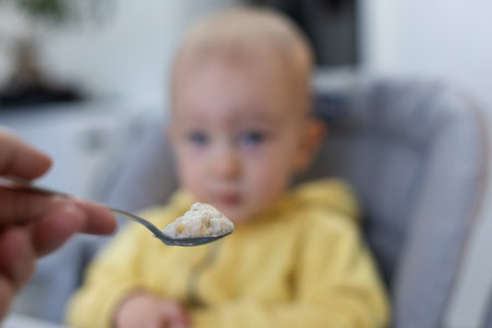 Toddler boy looking curiously at spoon of porridge. Selective focus.の写真素材