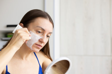 Woman in front of the mirror applying cream mask from a tube on her face.の写真素材