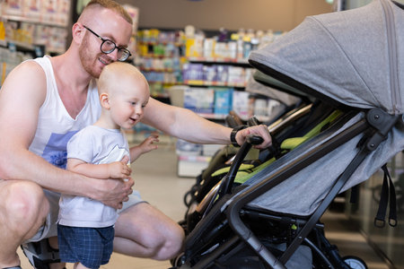Happy little kid together with his father choosing a baby troller in a children shop.