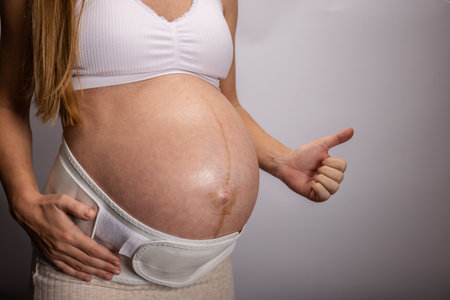 Closeup of pregnant woman on third trimester wearing support bandage for belly gesturing thumb up.