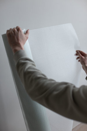 Male hands holding a roll of white plaster mesh for preparatory and painting works.の写真素材