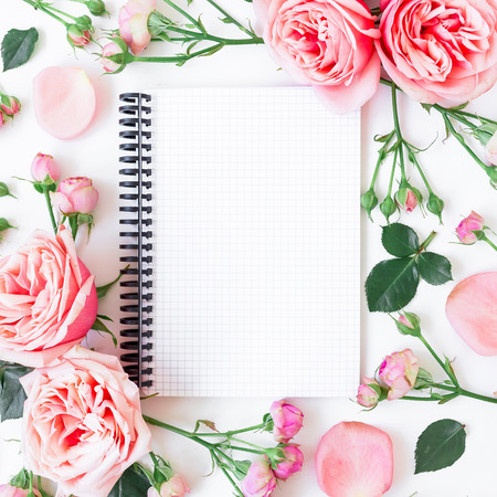 Floral frame made of pink roses, buds, petals, leaves and notebook on white background. Flat lay, Top view.の写真素材