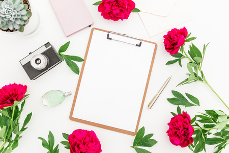 Beauty blog concept. Blogger or freelancer workspace with clipboard, notebook, retro camera, peonies and coffee mug on white background. Flat lay, top view.の写真素材