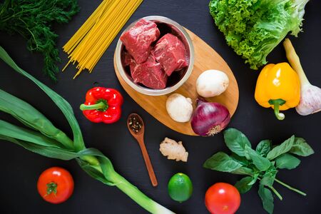 Raw meat in a plate on board, pasta and fresh vegetables on dark background. Top view. Flat lay. Food backgroundの写真素材