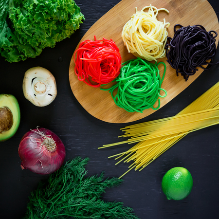 Multicolored pasta on a plate and vegetables isolated on a dark wood table. Flat lay. Top view. Food backgroundの写真素材