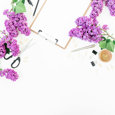 Freelance or blogger workspace with clipboard, notebook, scissors, lilac flowers and accessories on white background. Flat lay, top view. Beauty blog concept.の写真素材