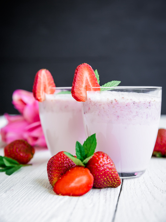 Strawberry smoothie with berries and pink flowers on white table and dark background. Fresh milkshakeの写真素材