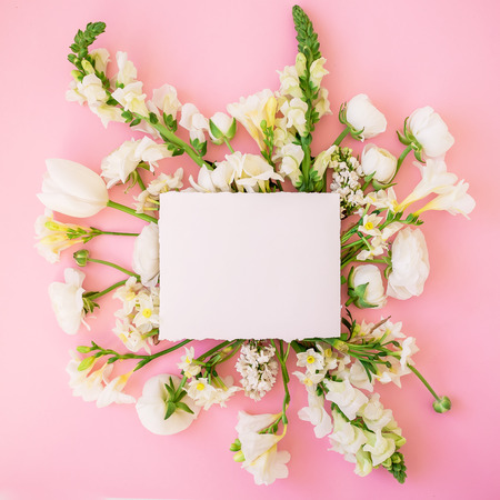 Frame of white flowers and paper card isolated on a pink background. Flat lay. Top viewの写真素材
