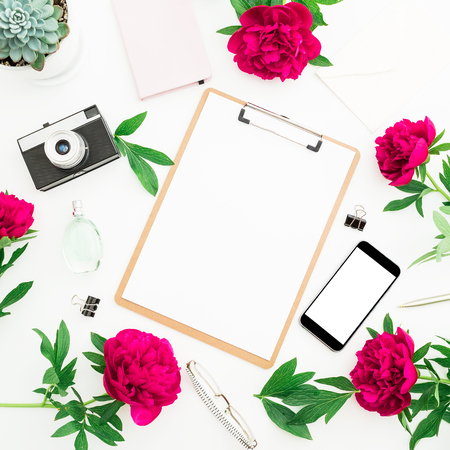 Beauty blog concept. Blogger or freelancer workspace with clipboard, notebook, retro camera, peonies and mobile phone on white background. Flat lay, top view.の写真素材