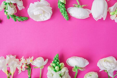 Floral frame made of white ranunculus, snapdragon, tulip and freesia flowers on pink background. Flat lay, top view. Pattern of flowers.の写真素材