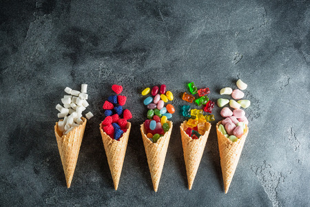 Colorful bright assorted candy in waffle cones on dark background. Flat lay, top view