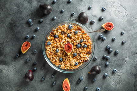 Healthy breakfast of muesli with nuts in a glass bowl, berries and fruits on a dark background. Flat lay, top viewの写真素材
