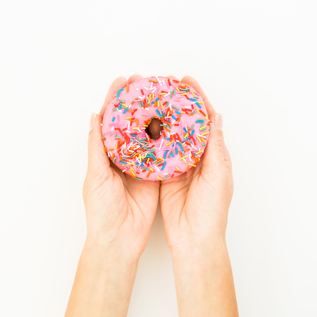 Colorful pink donut in woman hands. Delicious food. Flat lay, top viewの写真素材