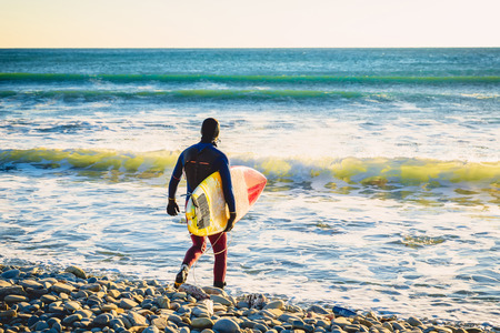 Surfer with surfboard on the beach at sunset or sunrise. Surfer and ocean wavesの写真素材