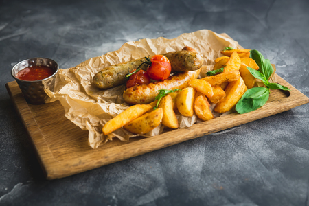 Fried sausages with potatoes and pickled tomato on a wooden plate. Closeup view.の写真素材