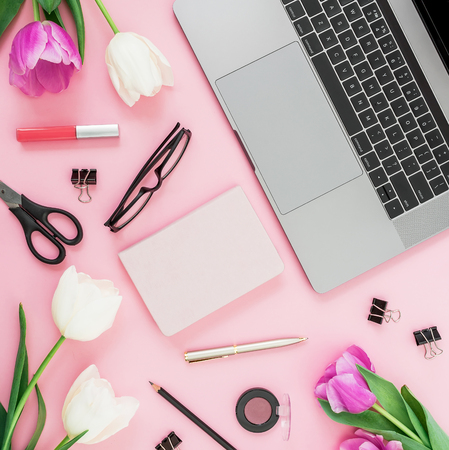 Workspace with laptop, tulips flowers, accessories and diary on pink background. Top view. Flat lay.の写真素材