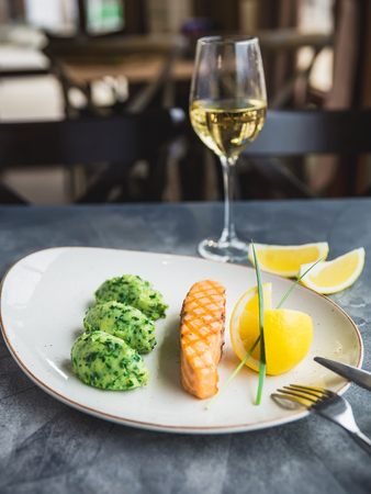 Dish with grilled salmon with lemon slices and glass of white wine on table. Close up viewの写真素材