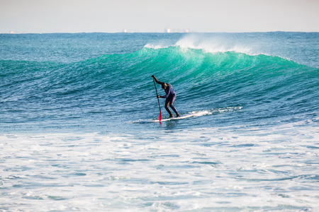 Surfer on stand up paddle board on blue wave. Winter surfing in oceanの写真素材